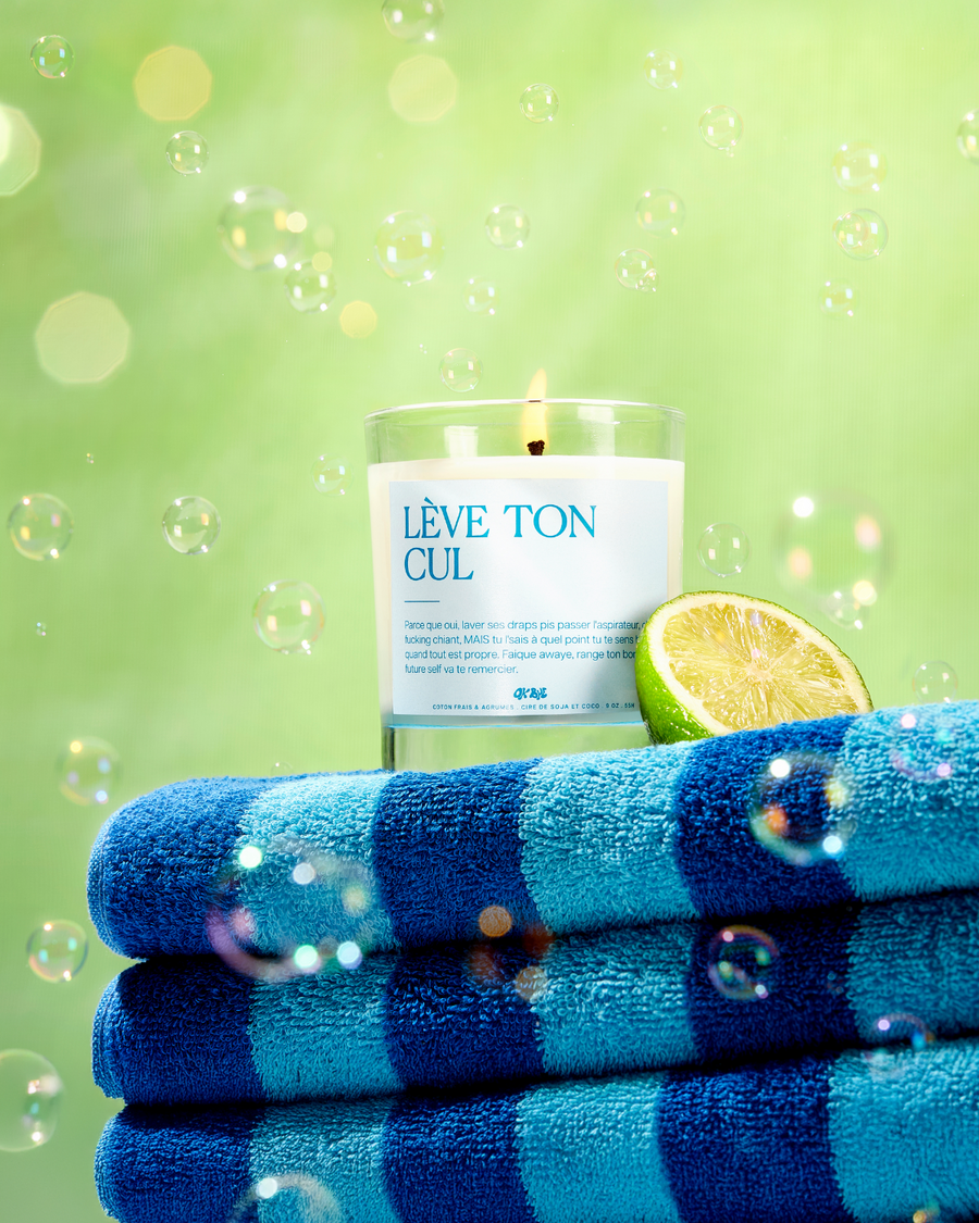 Bougie Coton Frais & Agrumes « Lève ton cul » allumée sur des serviettes rayées bleues