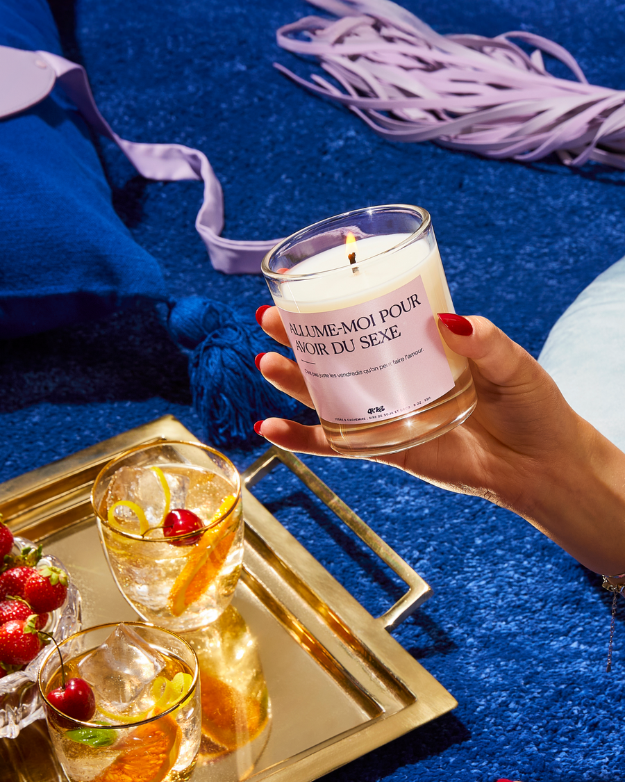Bougie Cèdre & Cachemire « Allume-moi pour avoir du sexe » tenue près d'un plateau de cocktails